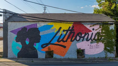 Colorful mural on a brick wall with silhouettes and the word Lithonia under power lines and blue sky.