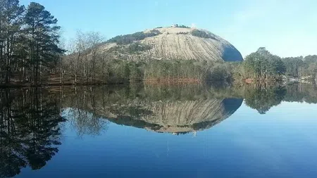 Stone Mountain reflected in calm lake water surrounded by autumn trees under a clear blue sky.