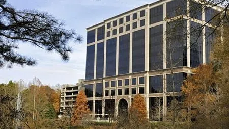Modern office building with reflective glass windows surrounded by trees in autumn near a pond.
