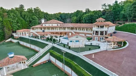 A large Mediterranean-style mansion with red tile roofs, surrounded by lush greenery and outdoor terraces.