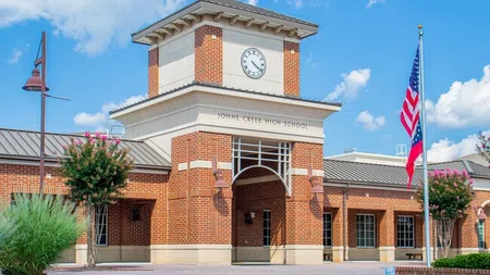Johns Creek High School brick building with clock tower and American flag against blue sky