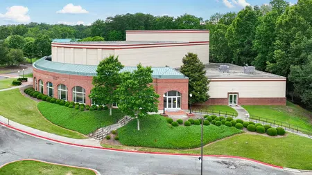 Modern brick and beige community building with green roof surrounded by trees and manicured landscaping in suburban area