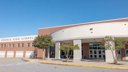 Entrance of Phoenix High School with brick facade, trees, and a clear blue sky.