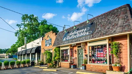 Antiques and collectibles store with brick facade and adjacent furniture restoration shop under a blue sky.