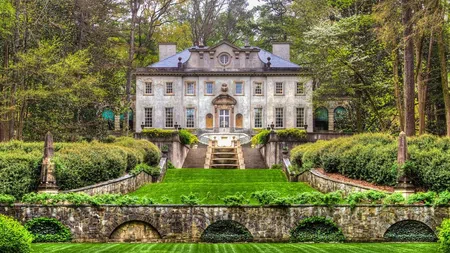 Historic mansion surrounded by lush greenery with manicured lawns and stone terraces in a woodland setting