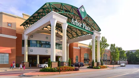 Entrance of Arbor Place shopping mall with people walking and cars parked under a green and white canopy