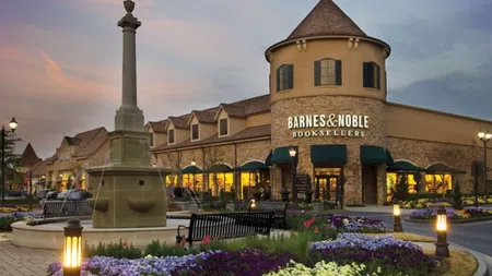 Barnes & Noble bookstore with a stone tower, flower garden, fountain, and evening lighting at sunset.