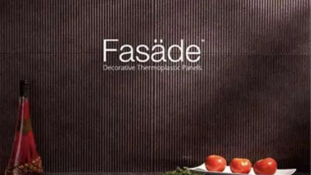 Decorative dark ribbed wall with Fasade text, tomatoes on white plate, herbs, and bottle on wooden surface.