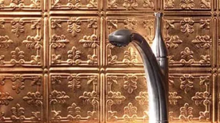 Modern silver faucet in front of decorative embossed copper backsplash tiles in kitchen or bathroom.