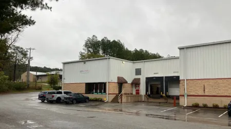 Exterior view of an industrial warehouse with loading docks and parked vehicles on a rainy day.