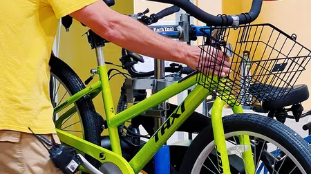 Man in yellow shirt adjusting a green taxi bike with a front basket indoors near Cocoa Beach Bicycle Company logo.