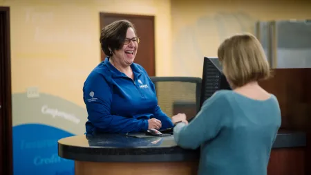 Smiling customer service representative assisting a client at a bank counter with computer and documents