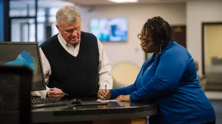 Man and woman discussing and writing at office counter with computer in business environment
