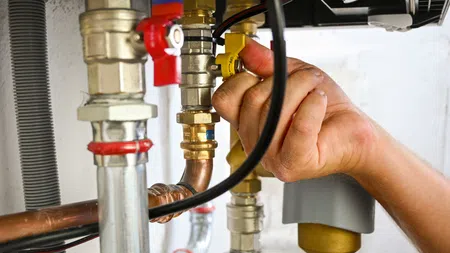 Hand adjusting a valve on a copper plumbing system with pipes and connectors in a utility area.