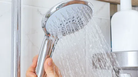 Hand holding a chrome shower head with water flowing in a bright modern bathroom
