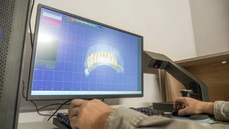 Person designing a 3D dental model on a computer screen using specialized software in a dental lab.