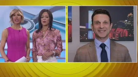 Two female news anchors and a male correspondent in a split-screen live broadcast with cityscape background.