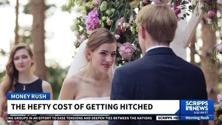 Bride and groom exchange vows under floral arch during outdoor wedding ceremony with bridesmaid in background.