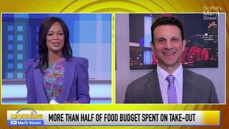 Two hosts discuss food budget spending with a text banner on take-out expenses on a TV show set.