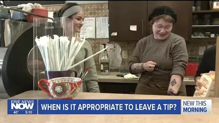 Two smiling women behind a coffee shop counter with straws and a decorative cup in front