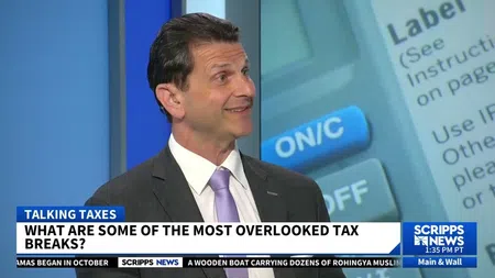 Man in suit discusses overlooked tax breaks on Scripps News segment with tax-related graphics in background