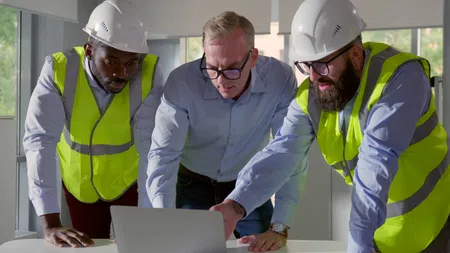 a group of men wearing hardhats looking at a laptop