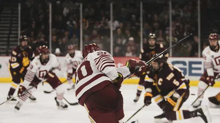 Ice hockey player in red and white shooting puck amid opposing players during a game in an indoor rink