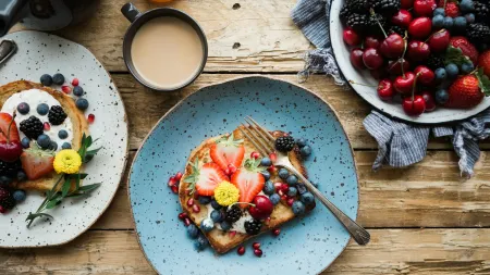 French toast topped with fresh strawberries, blueberries, blackberries, and edible flowers on rustic plates with coffee.