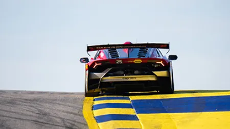 Rear view of a racing car with spoiler on a track curving over yellow and blue striped curbs.