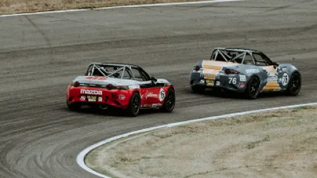 Two Mazda Miata race cars speeding on a curved racetrack during a competitive motorsport event.