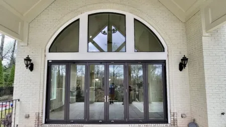 Modern glass double doors with black frames set in a white brick wall under an arched window with outdoor wall lanterns