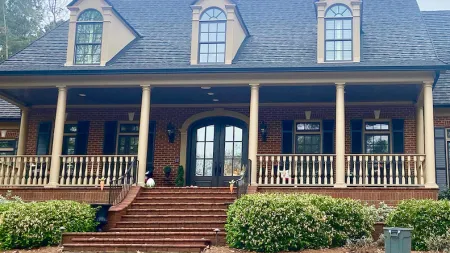 Brick house with large porch, six columns, dormer windows, front steps, and landscaped yard with curved driveway.