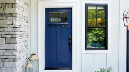 Front porch with dark blue modern door, white frame, stone wall, black window, and outdoor lanterns.
