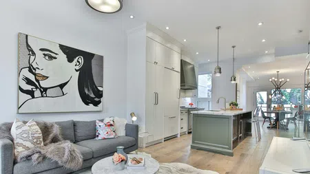 Modern open living space with gray sofa, pop art wall, kitchen island, and light wood flooring in bright home.
