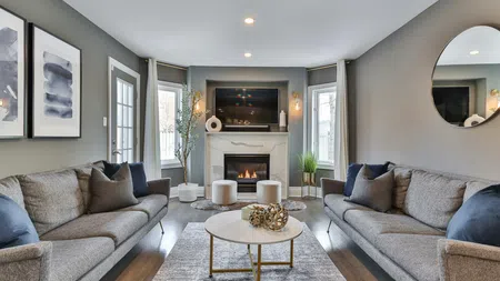 Modern living room with gray sofas, fireplace, wall art, round mirror, and a white coffee table on a rug