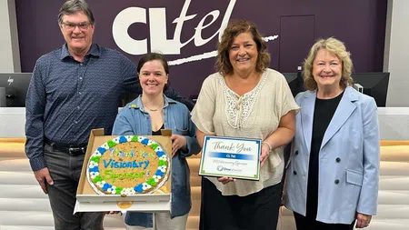 Four people standing inside the CL Tel office holding a thank you cookie and appreciation plaque for visionary sponsorship.