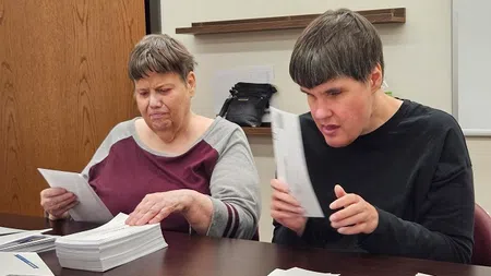 Two adults sorting and inspecting paper ballots at a table in an indoor setting