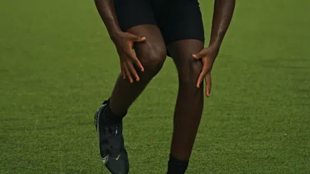 Athletic young man in a white tank top and black shorts running outdoors on grass with intense focus.