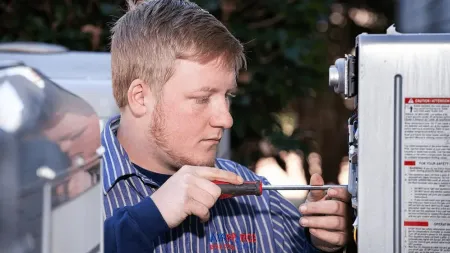 Technician with red screwdriver repairing electrical equipment outdoors, focused on wiring and components.
