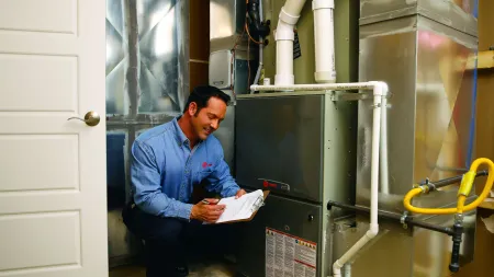 Technician inspecting and taking notes on a residential furnace system in a basement utility room.