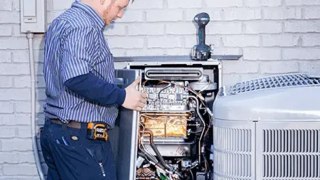 Technician inspecting and repairing an outdoor HVAC unit against a white brick wall background.