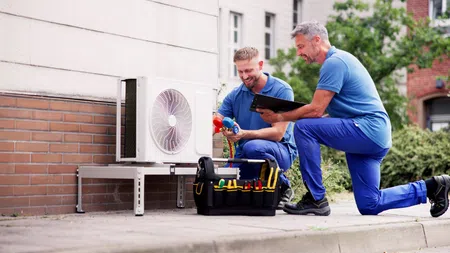 Technicians installing and inspecting an outdoor air conditioning unit with tools and clipboard.