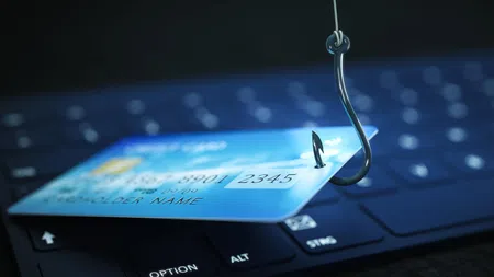Credit card pierced by a fishing hook on a keyboard symbolizing online fraud and phishing scams.