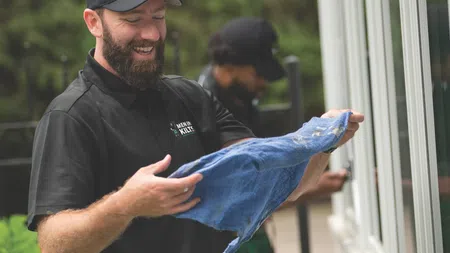 Smiling man in Men in Kilts uniform holding a cleaning cloth near a window outdoors