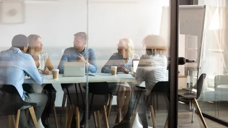 Five diverse professionals discussing work around a conference table in a modern office meeting room.