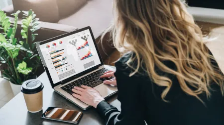Person working on laptop analyzing colorful business charts with coffee cup and smartphone nearby