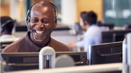 Smiling man wearing headset working at computer in busy call center environment
