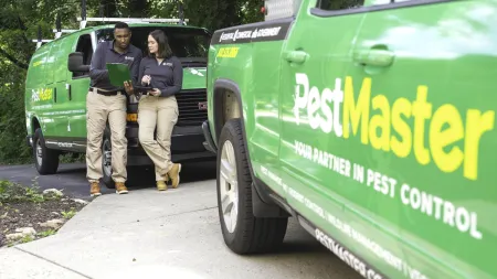 Pest control professionals reviewing documents beside green Pest Master service vehicles in outdoor setting.