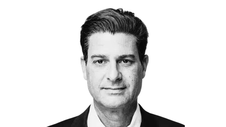 Black and white portrait of a man with dark hair wearing a suit jacket and white shirt looking straight ahead.