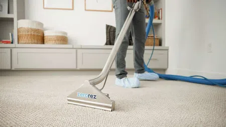 Professional carpet cleaning with Zerorez equipment in a modern living room, person in protective shoe covers.